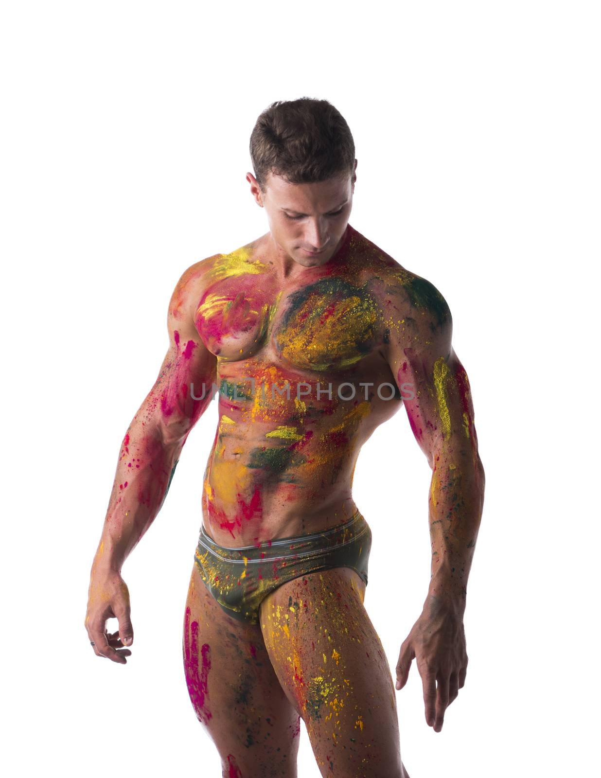 Muscular young man shirtless with skin painted with Holi colors, looking down, isolated on white