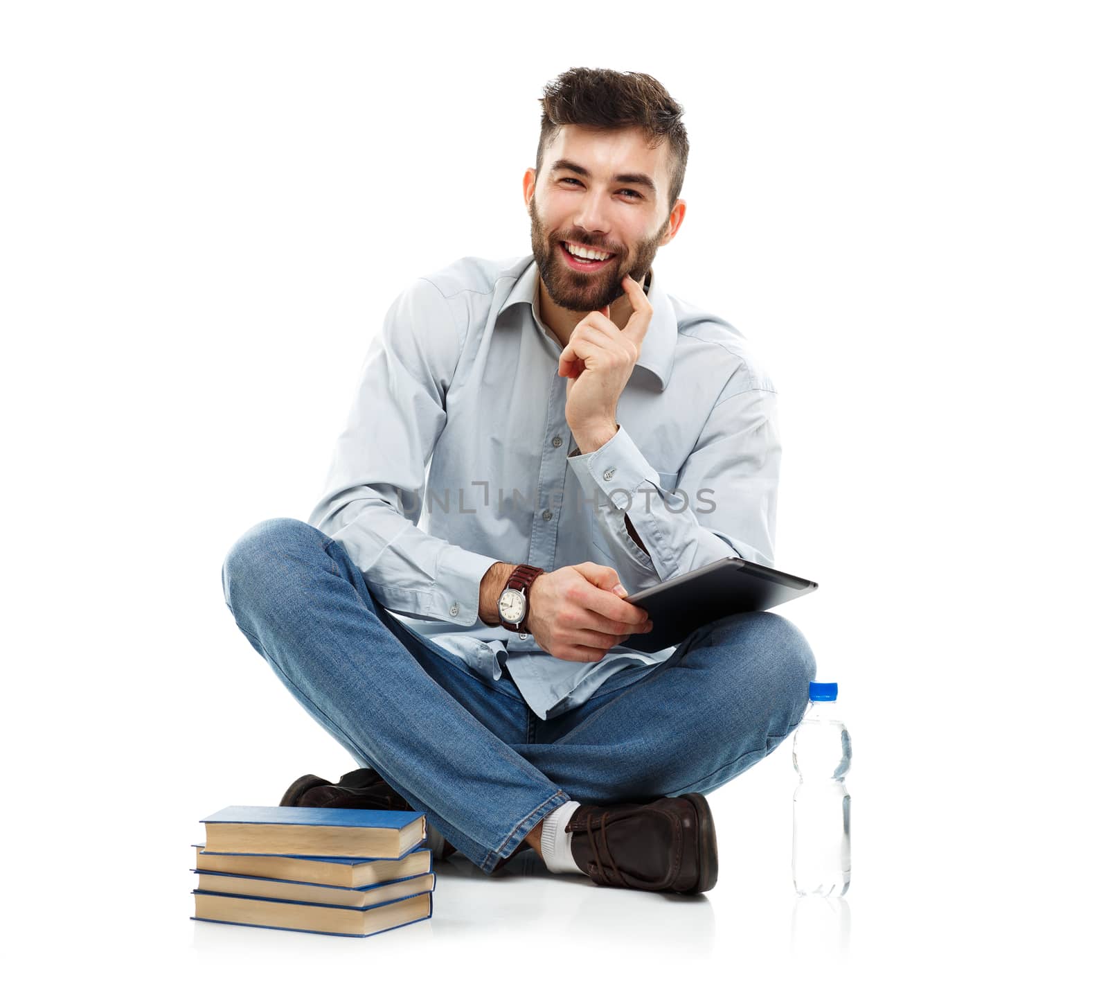 Young bearded smiling man holding a tablet with books and a bottle of water sitting on a white background