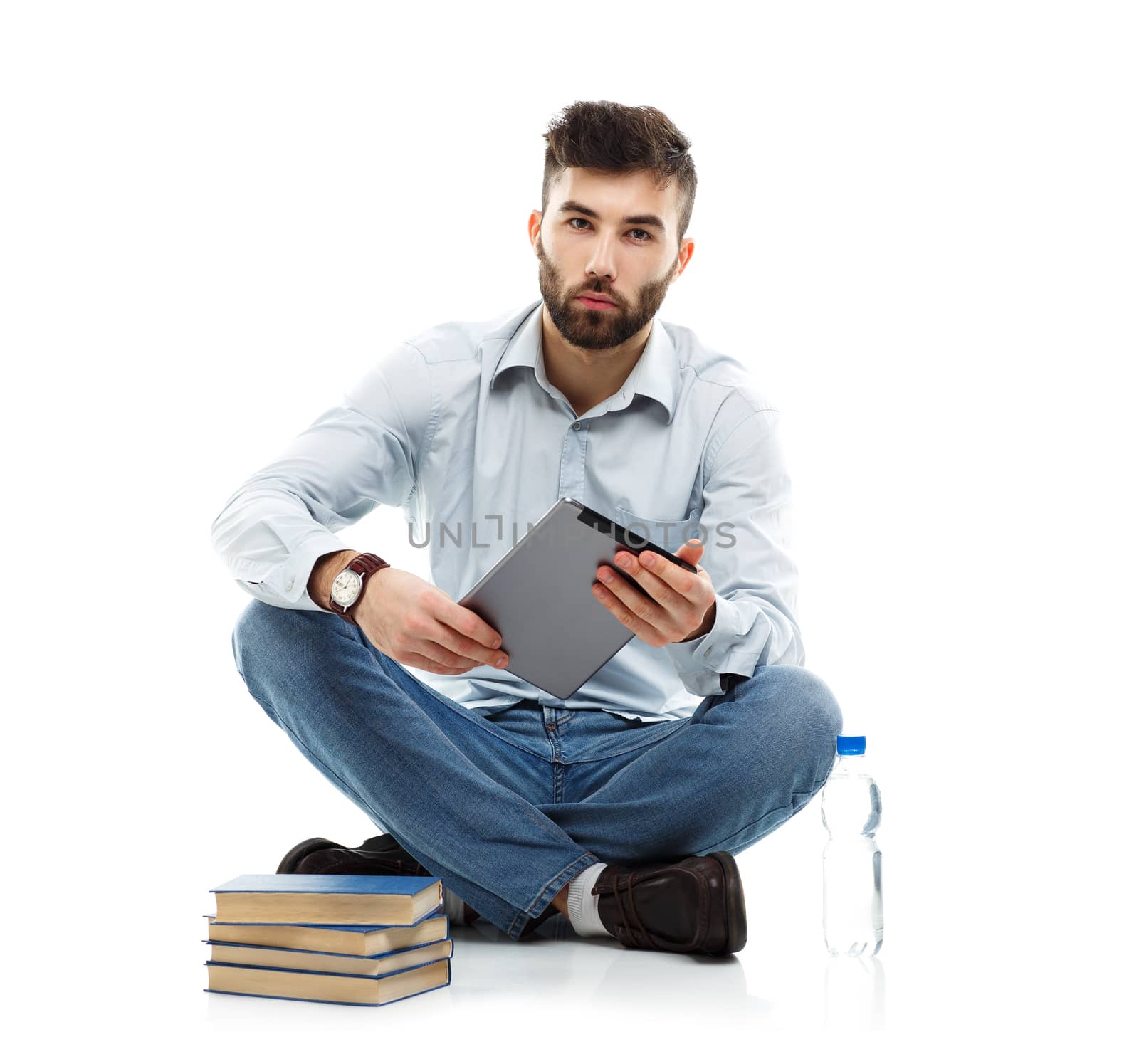 Young bearded smiling man holding a tablet with books and a bottle of water sitting on a white background