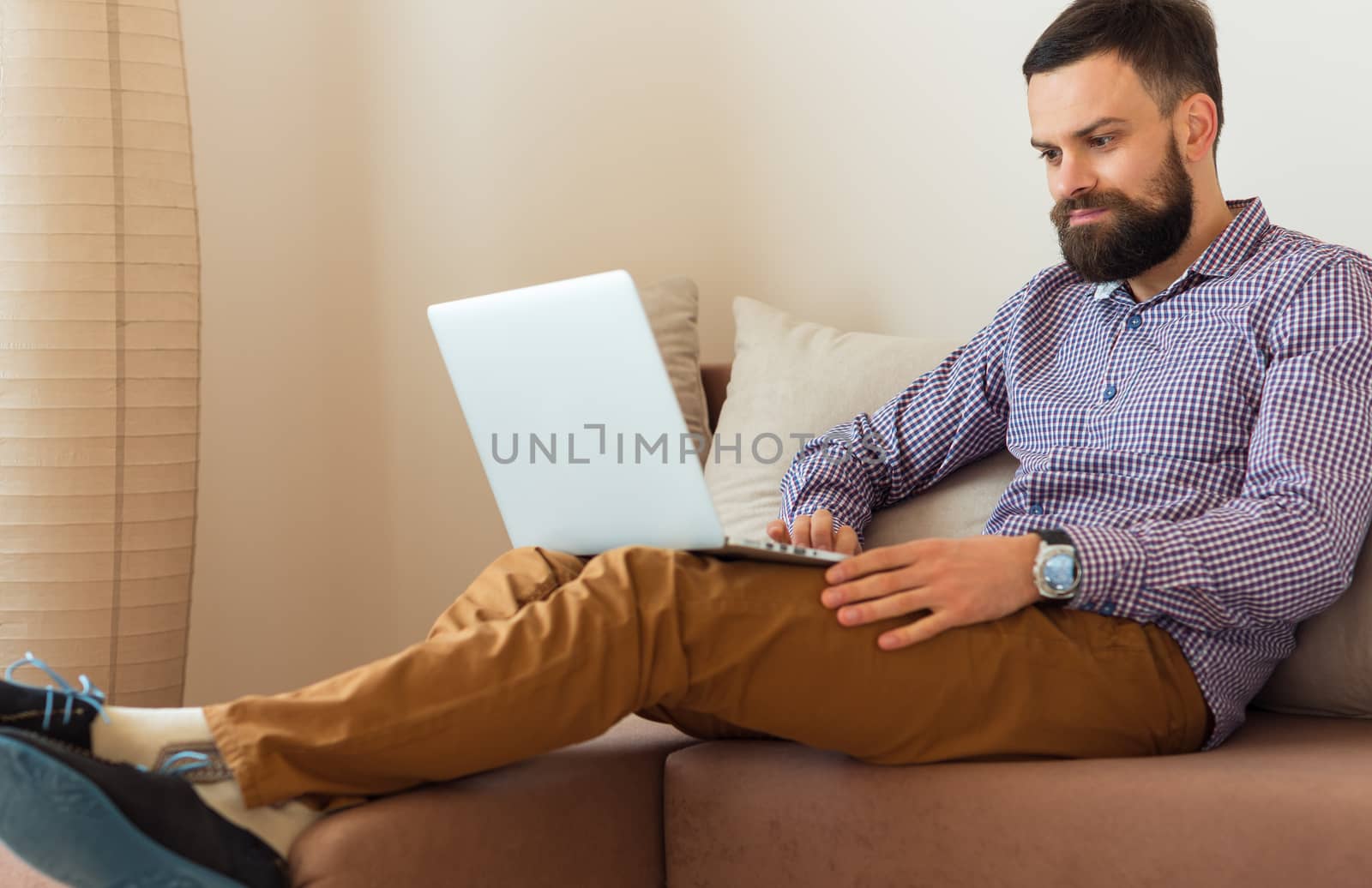 Young bearded man working on laptop at home by vlad_star