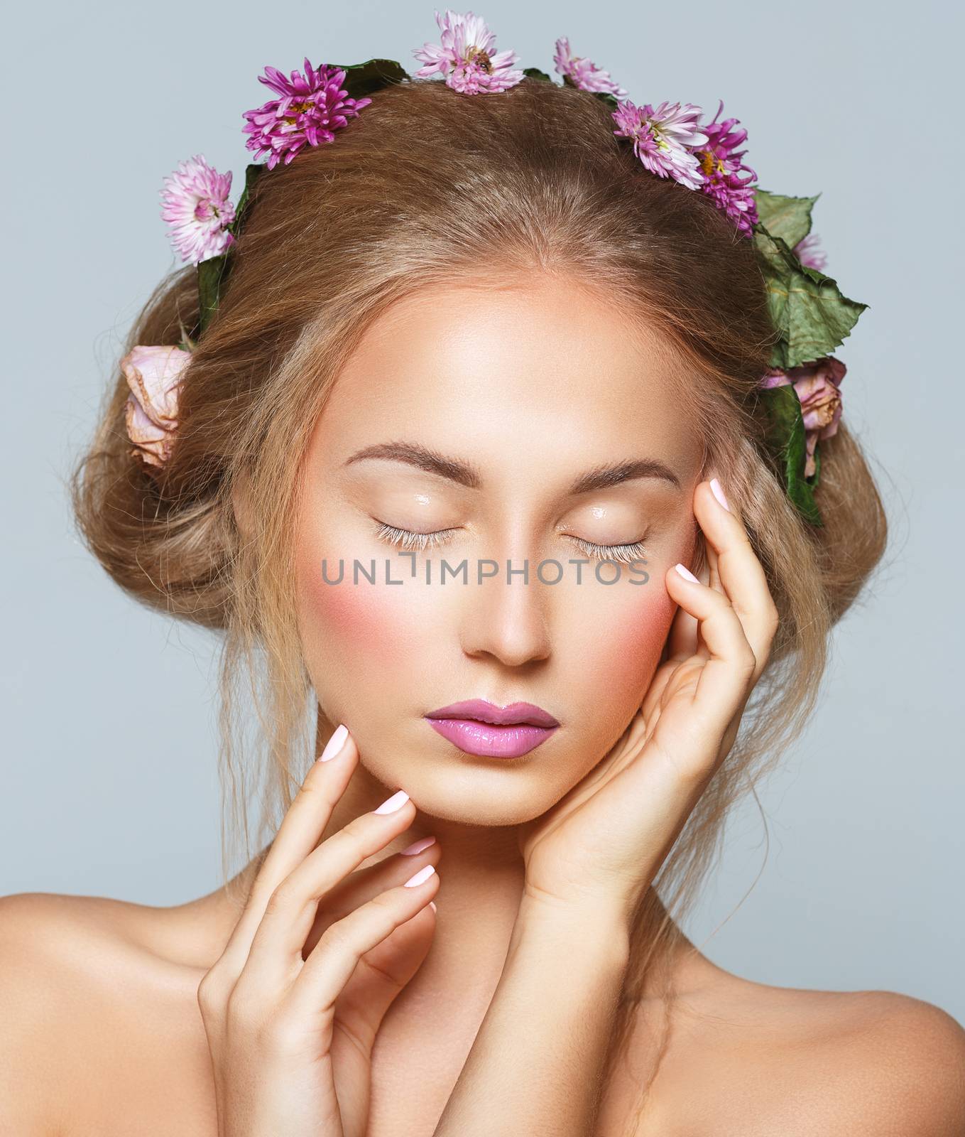 Lovely model with shiny volume curly hair with flowers, winter white eyelashes make-up, vivid lips and pink cheeks. Christmas look