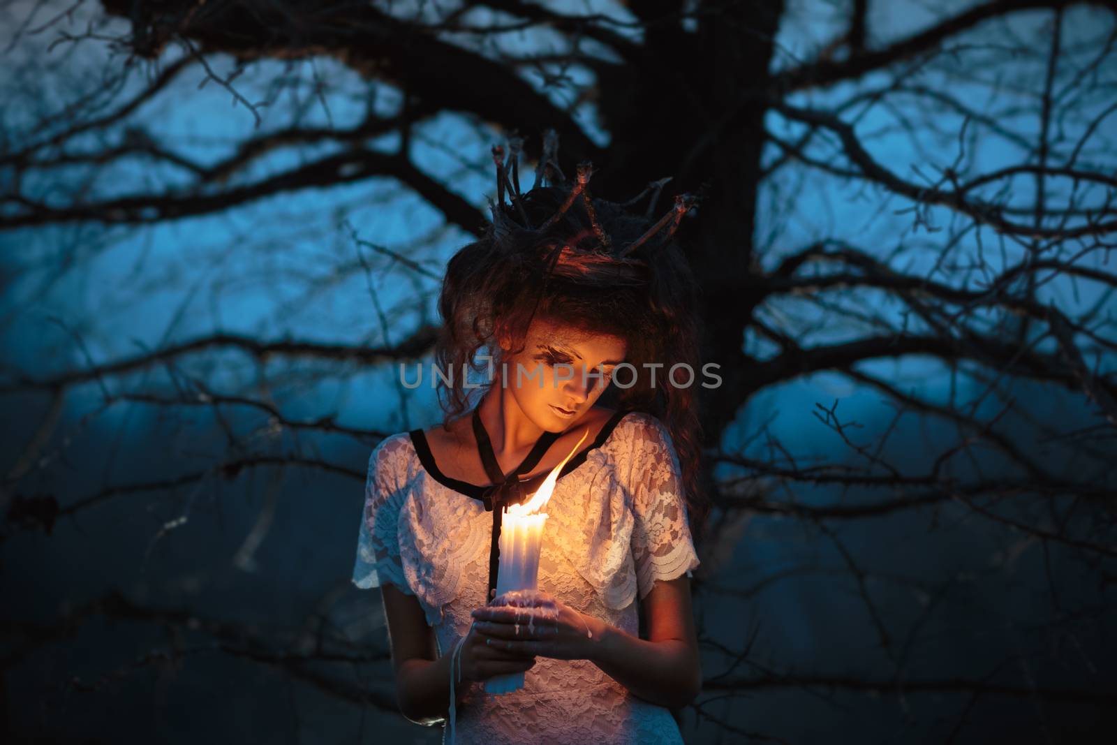 Young girl in the image of a bride in a white lace dress, a crown of twigs with lighted candles in their hands