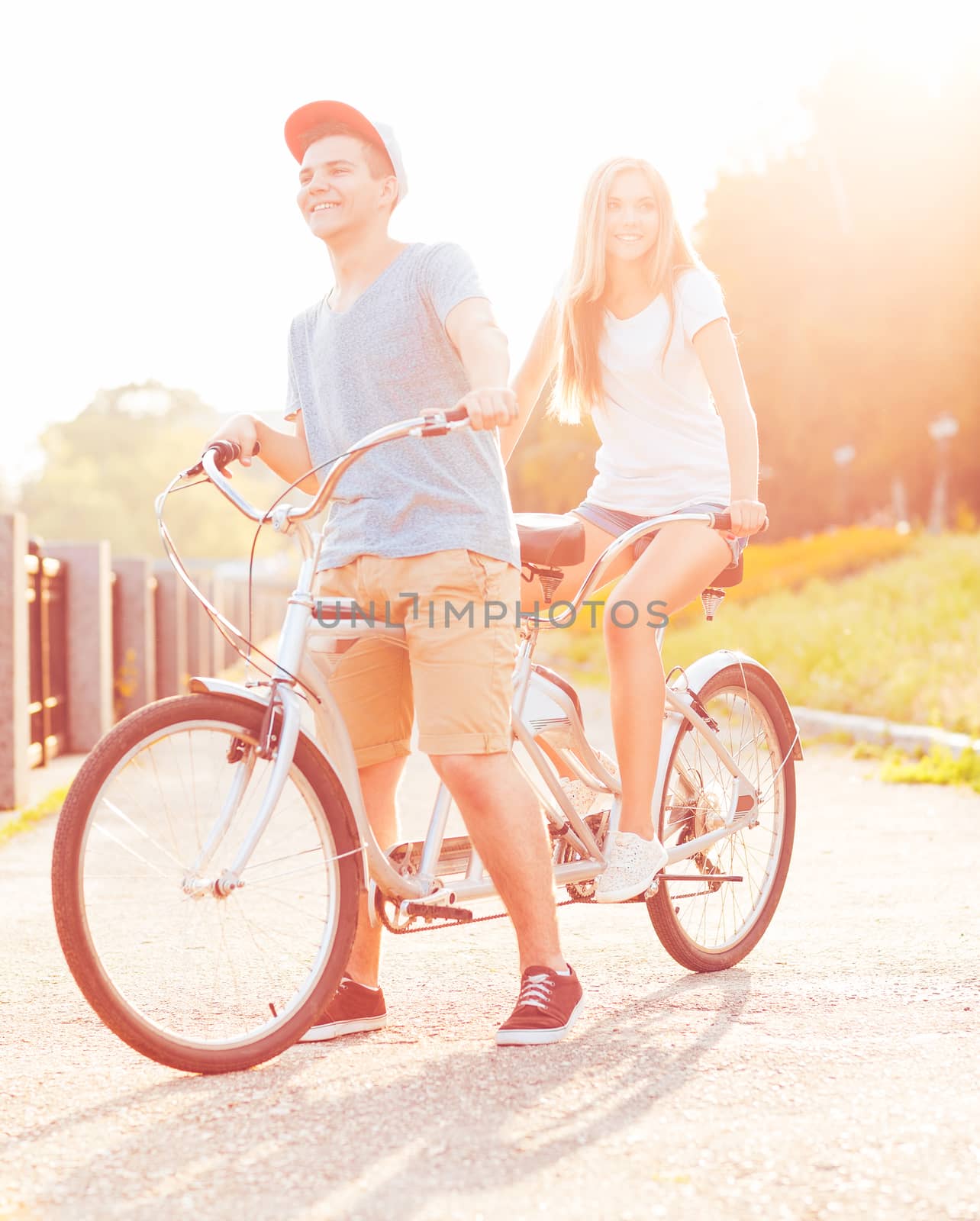 Happy couple - young man and woman riding a bicycle in the park outdoors