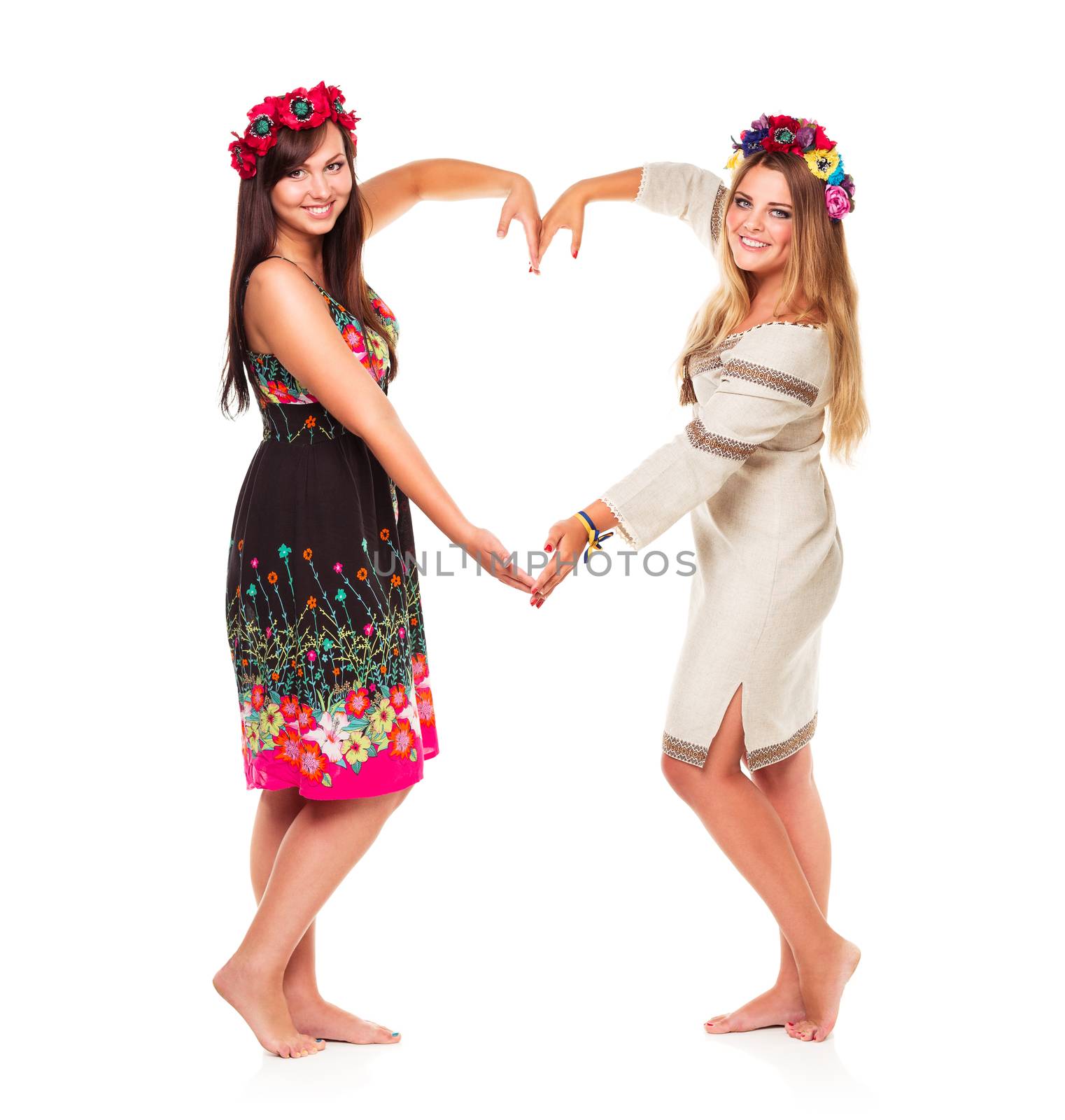 Two beautiful laughing girl in Ukrainian national costumes show heart shape hands on a white background