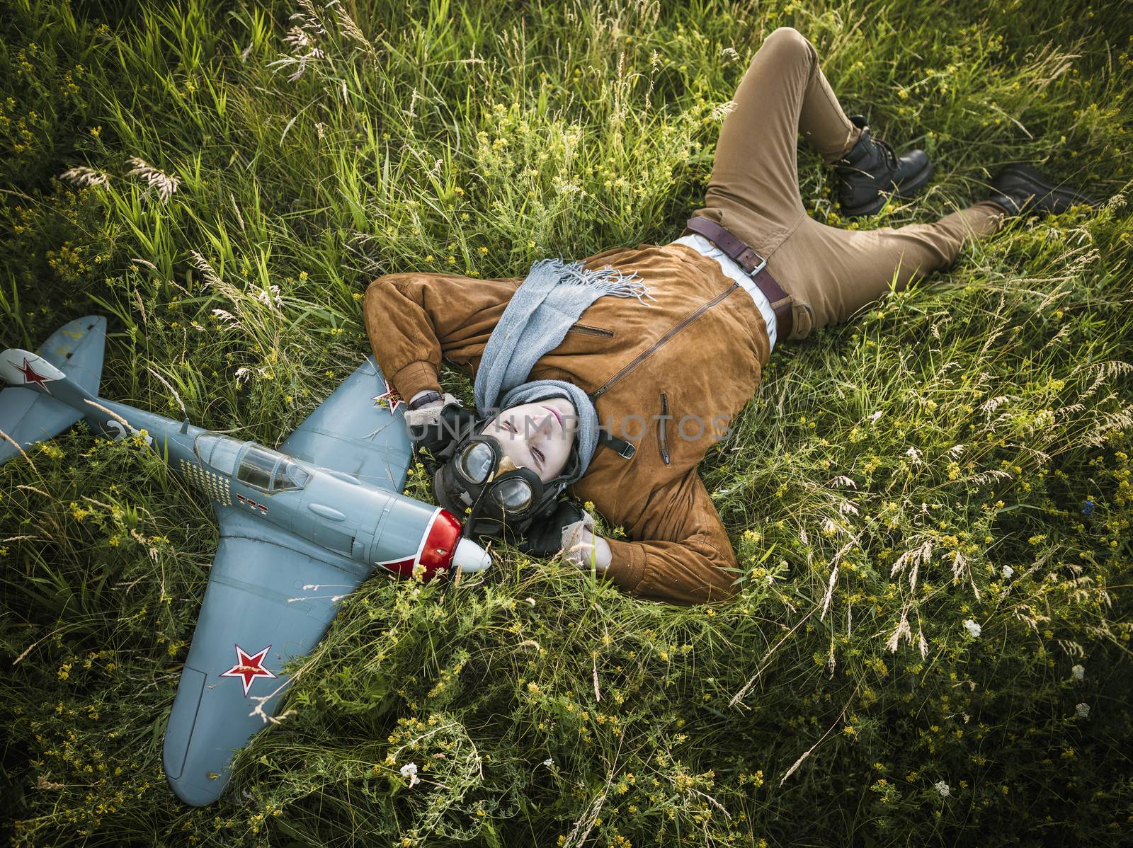 Young guy in vintage clothes pilot with an airplane model lies in the grass outdoors