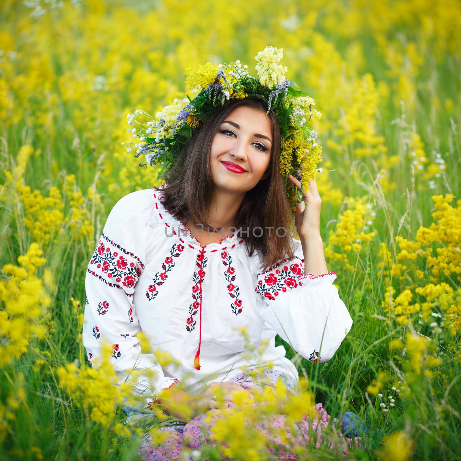 Young beautiful smiling girl in Ukrainian costume with a wreath on his head in a meadow