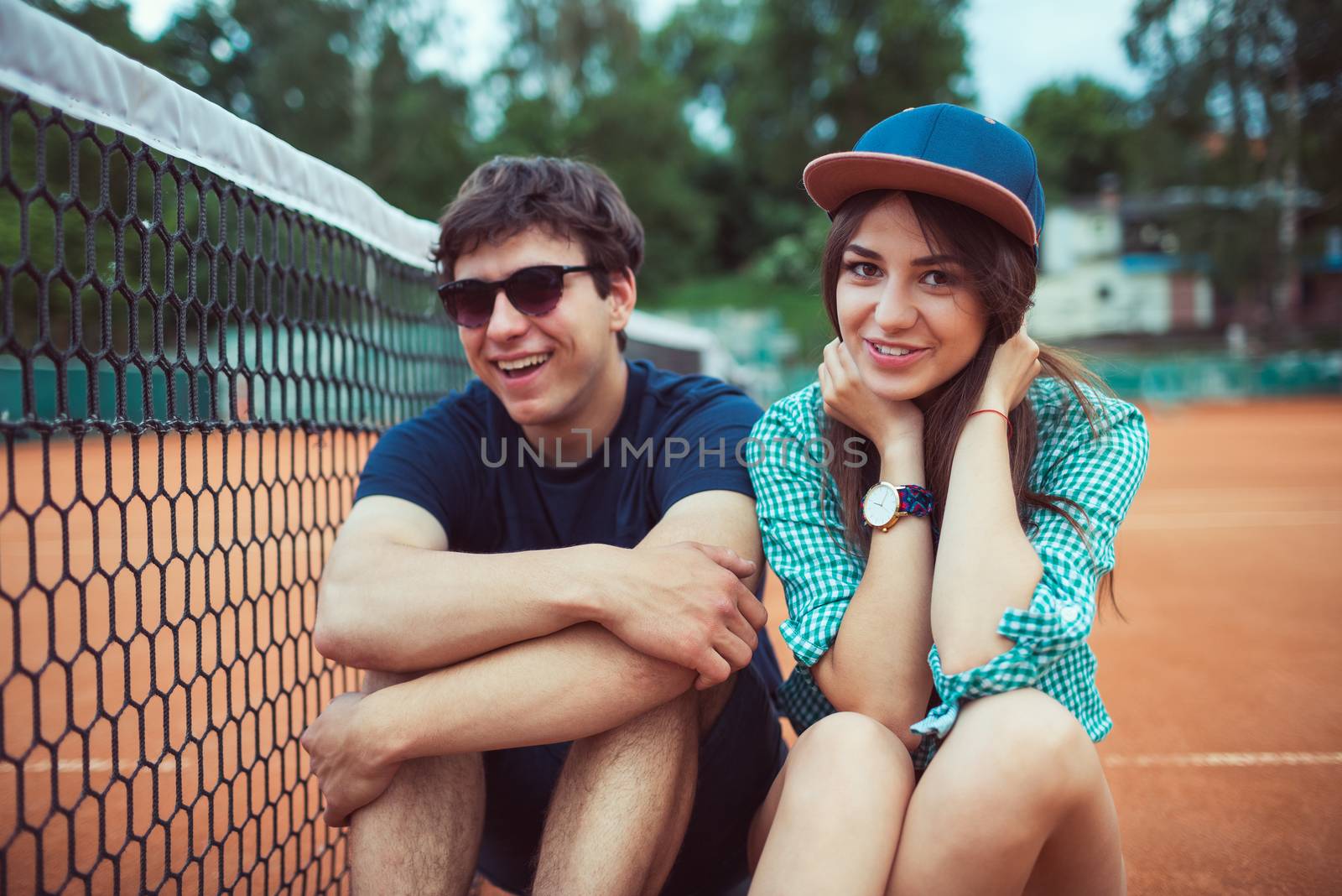 Young couple sitting on a skateboard on the tennis court by vlad_star
