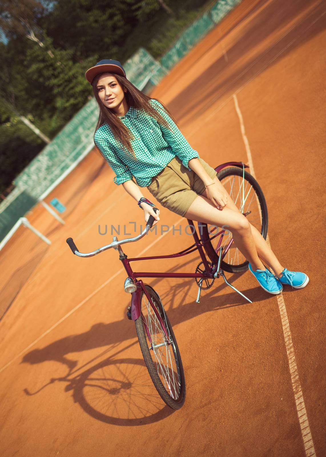 Girl hipster standing with magenta bike on the tennis court. Outdoor lifestyle portrait