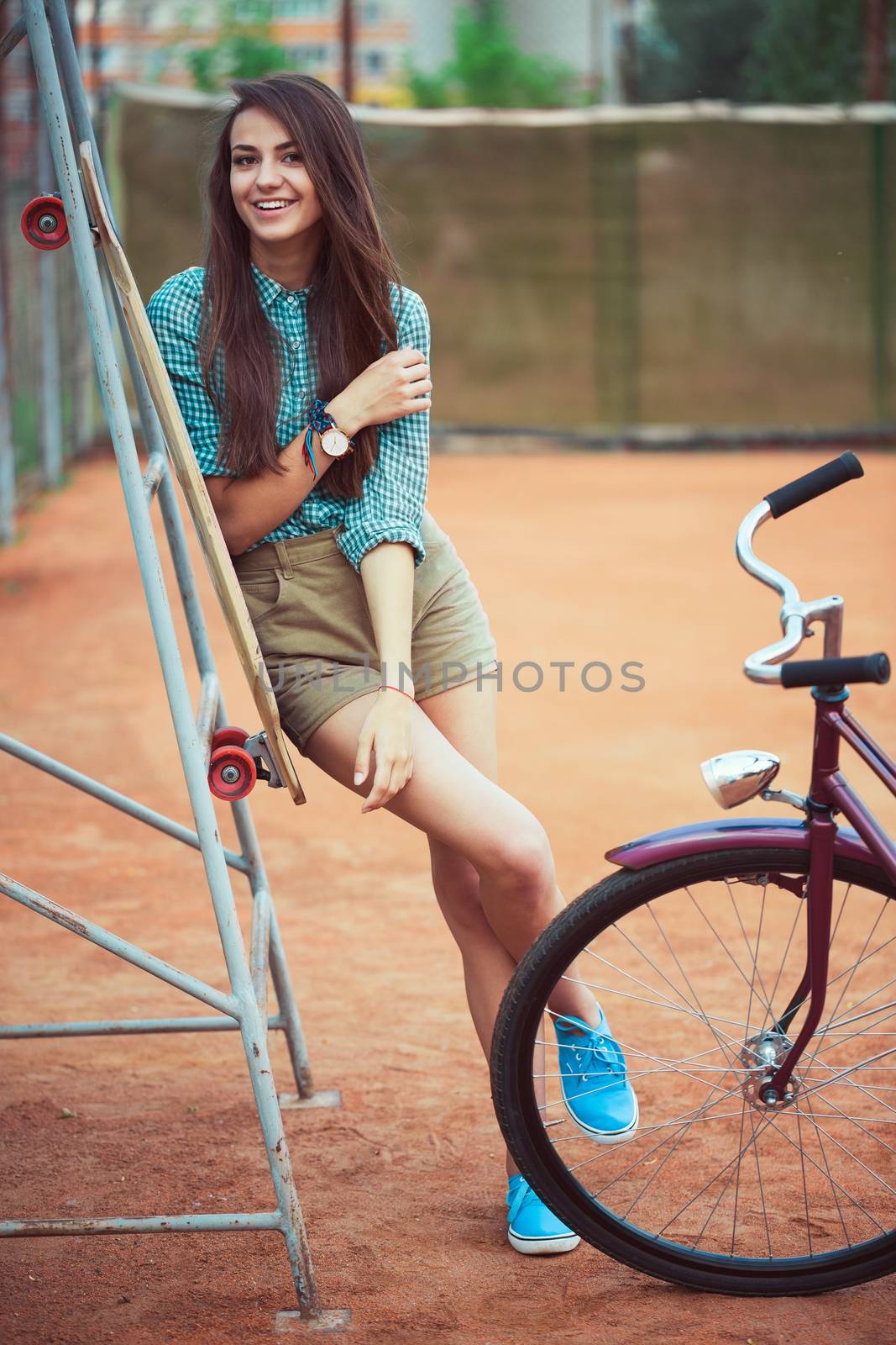 Beautiful young girl with longboard and bicycle standing on the tennis court, outdoor