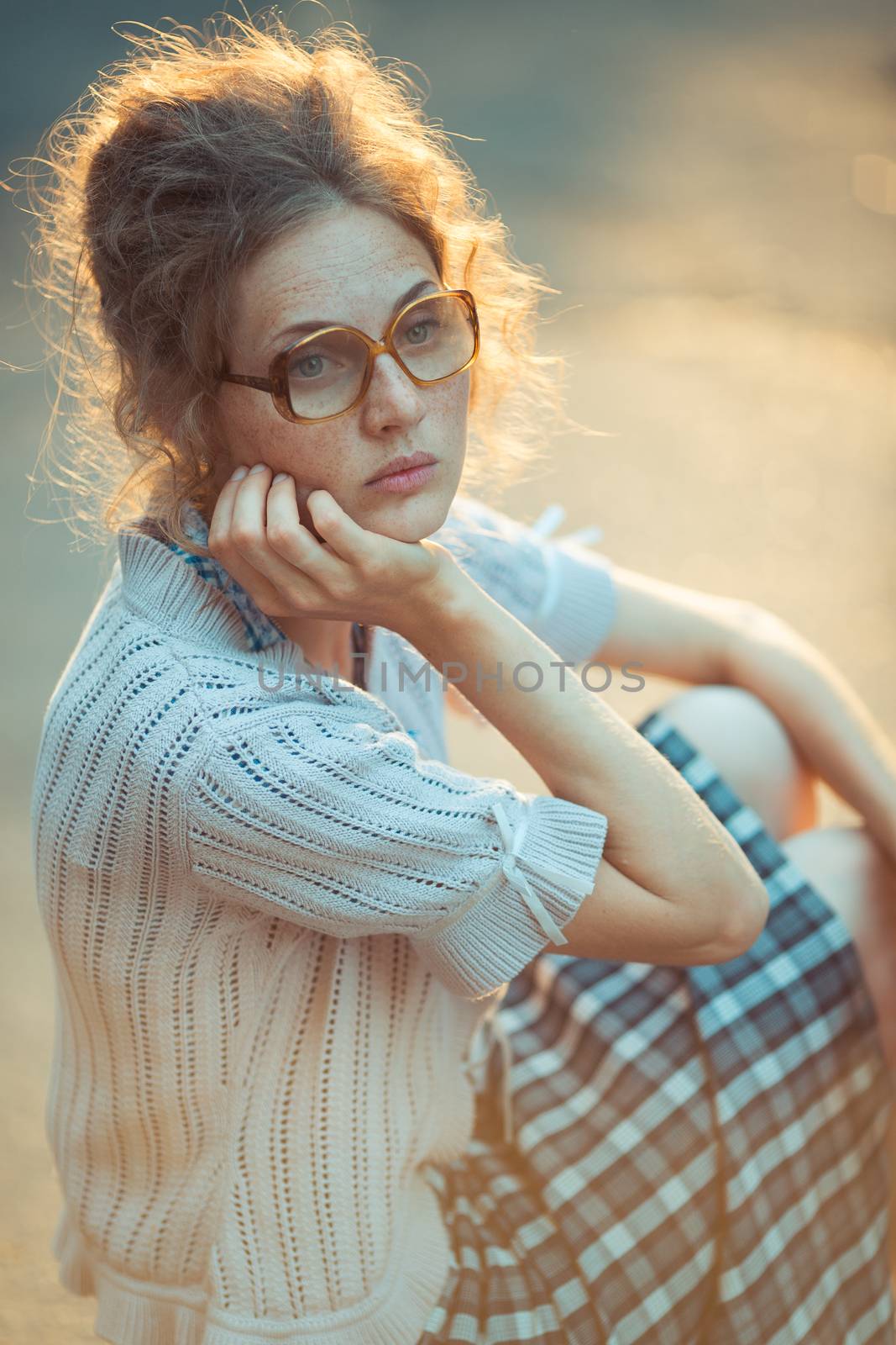 Funny girl student with glasses and a vintage dress sitting outdoors with a thoughtful look