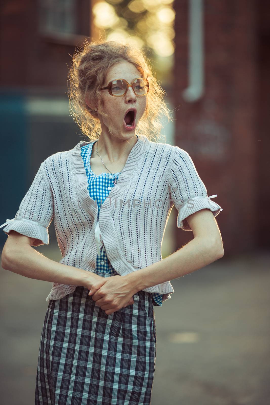 Funny crazy girl student in glasses and a vintage dress talking with his mouth wide open outdoors