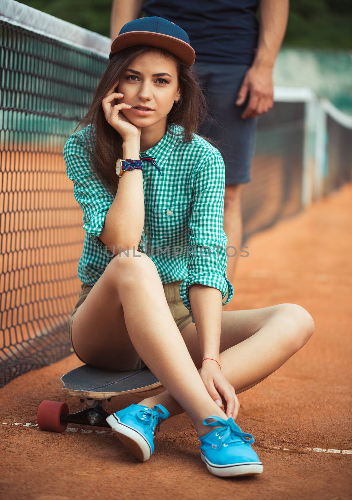Young beautiful girl sitting on a skateboard on the tennis court