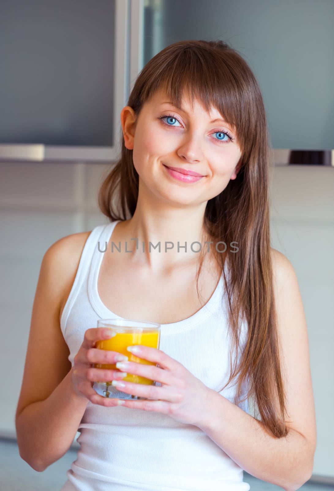 Young caucasian brunette girl with a glass of juice in the kitchen