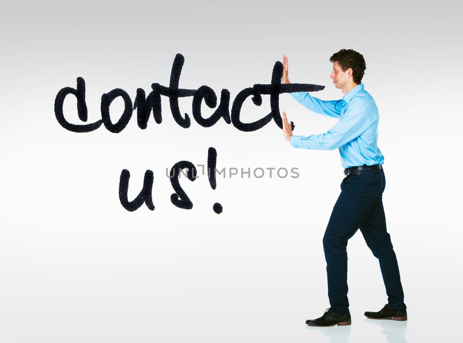 Young businessman with a card Contact Us on a grey background