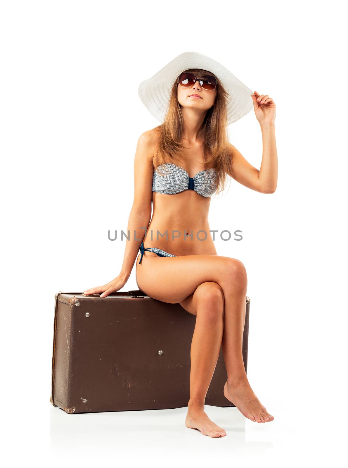 Full length portrait of a beautiful young woman posing in a bikini sitting on a suitcase on a white background