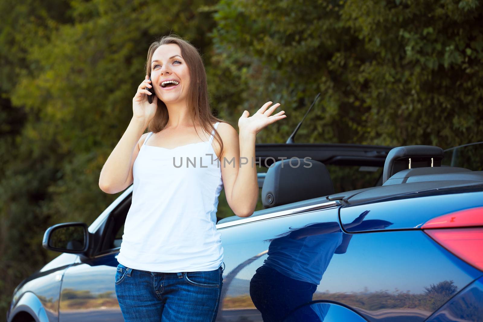 Happy caucasian girl on a cell phone service or tow truck traffic near the cabriolet car