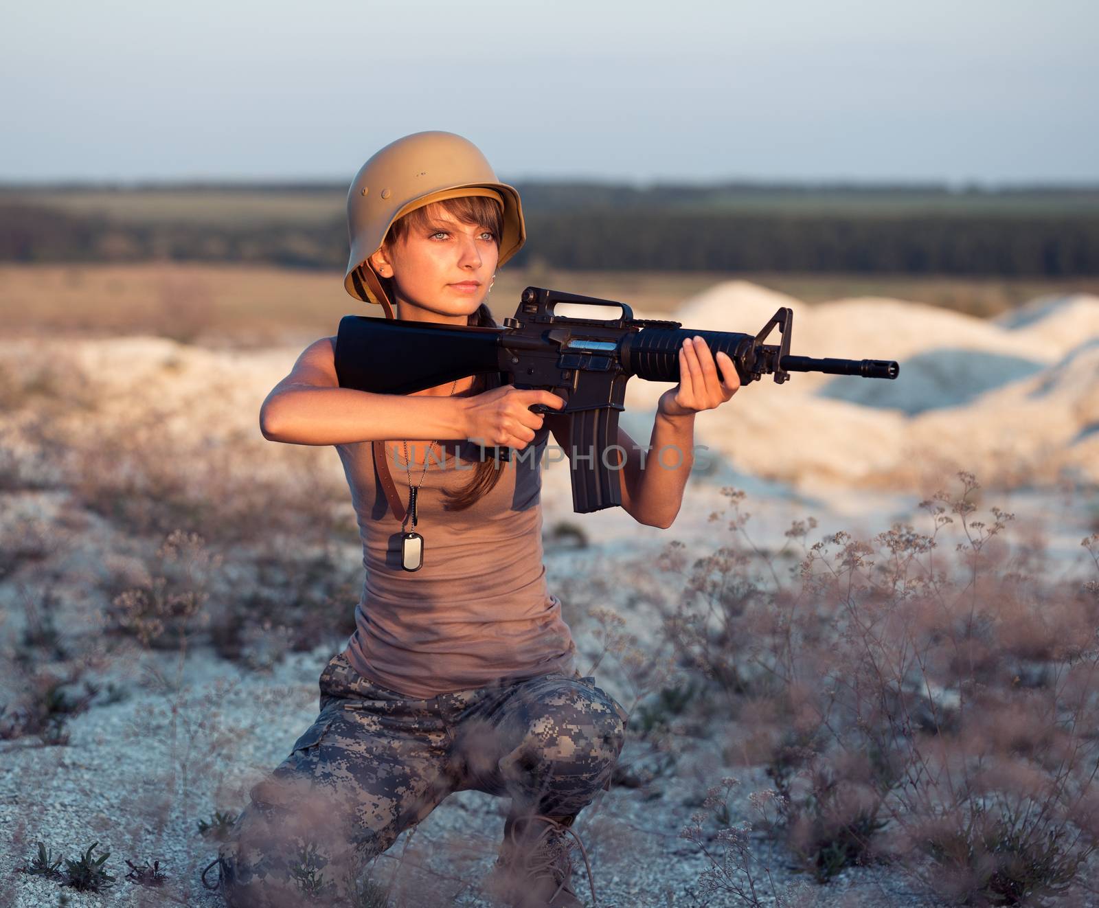 Young beautiful female soldier dressed in a camouflage with a gun in the outdoor