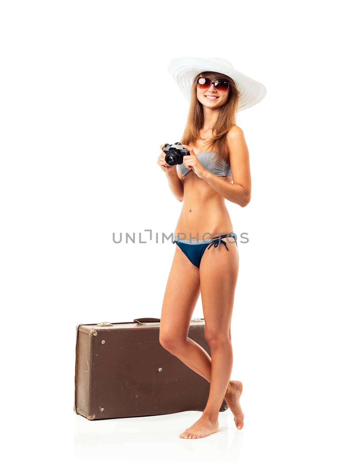 Full length portrait of a beautiful young woman posing in a bikini with a camera in hands and suitcase on white background