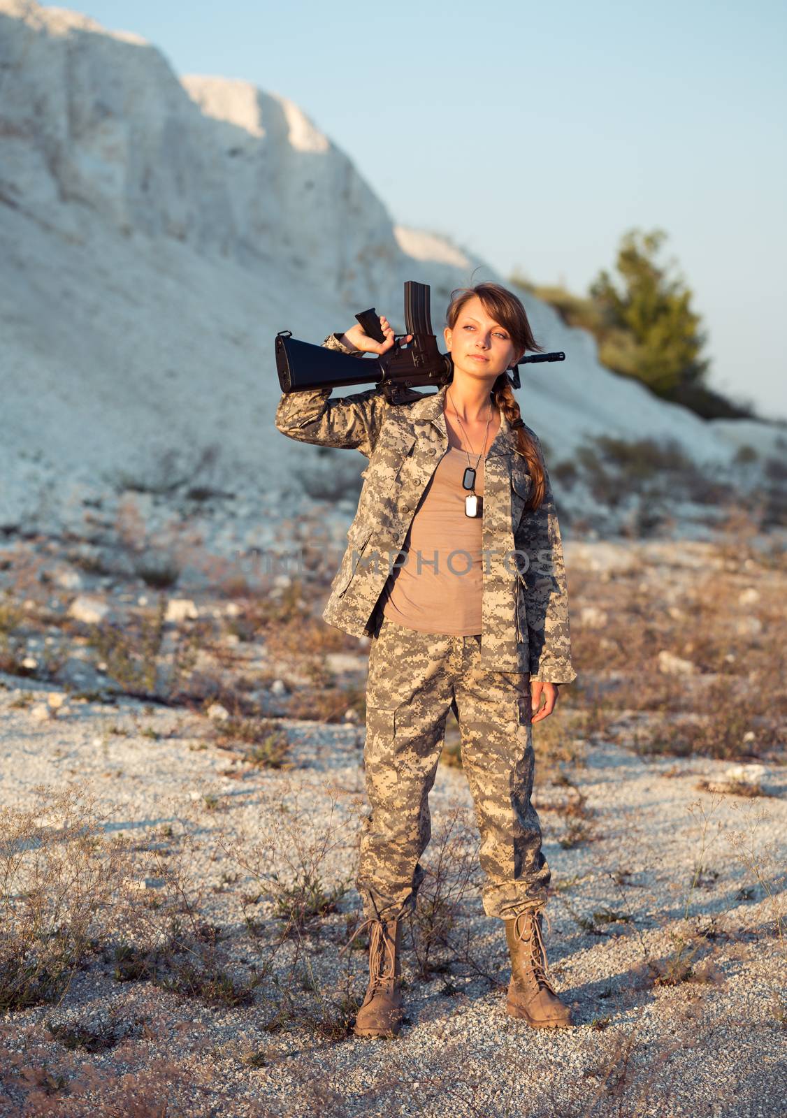 Young beautiful female soldier dressed in a camouflage with a gun in the location