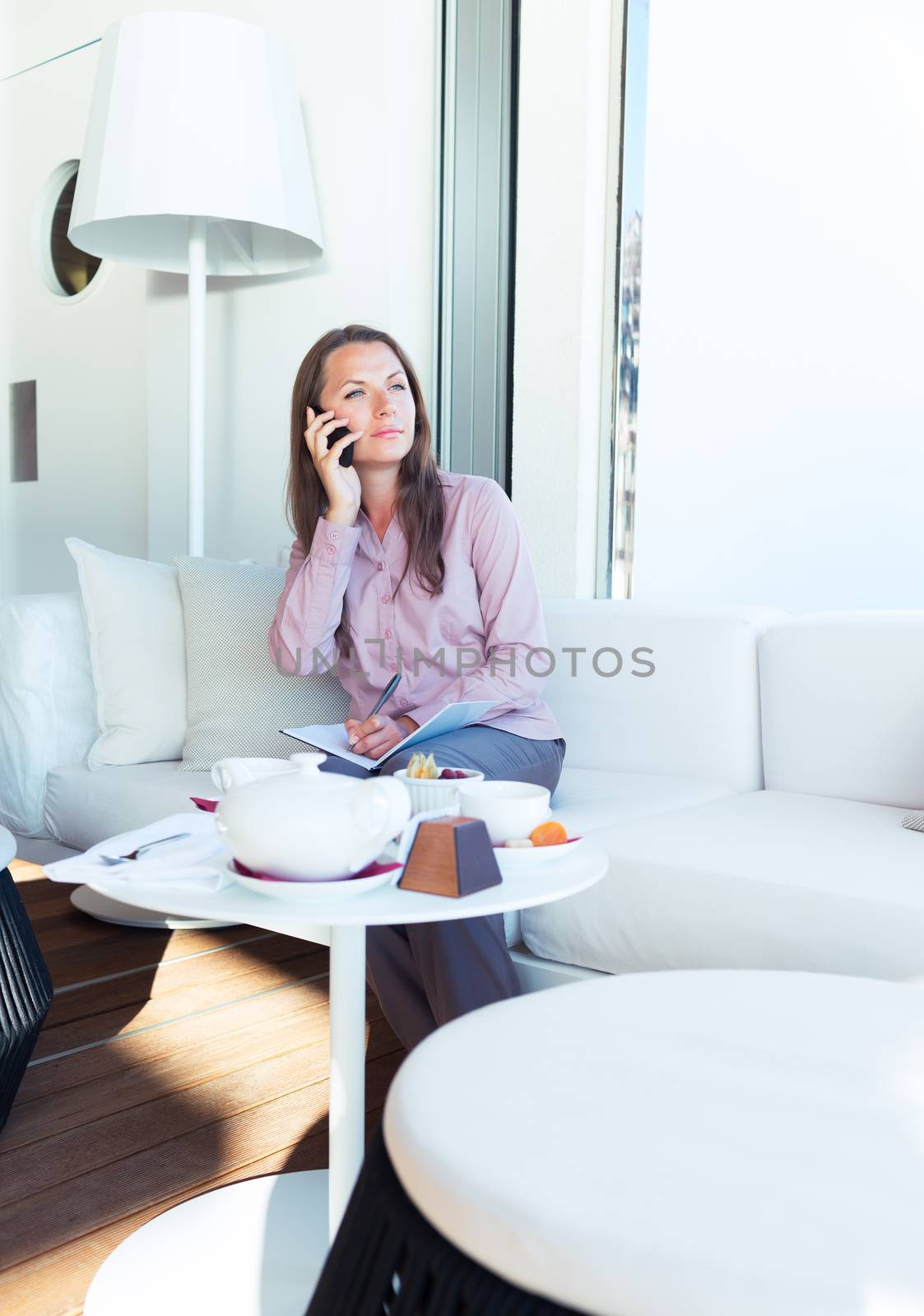 Businesswoman talking on the cellphone and writing in organizer in a coffee house