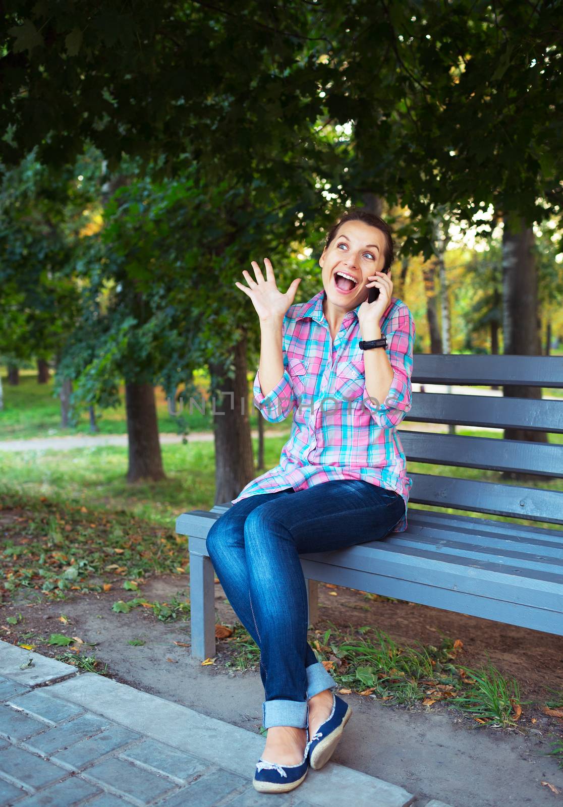 A portrait of a smiling beautiful woman in a park on a bench talking on the phone