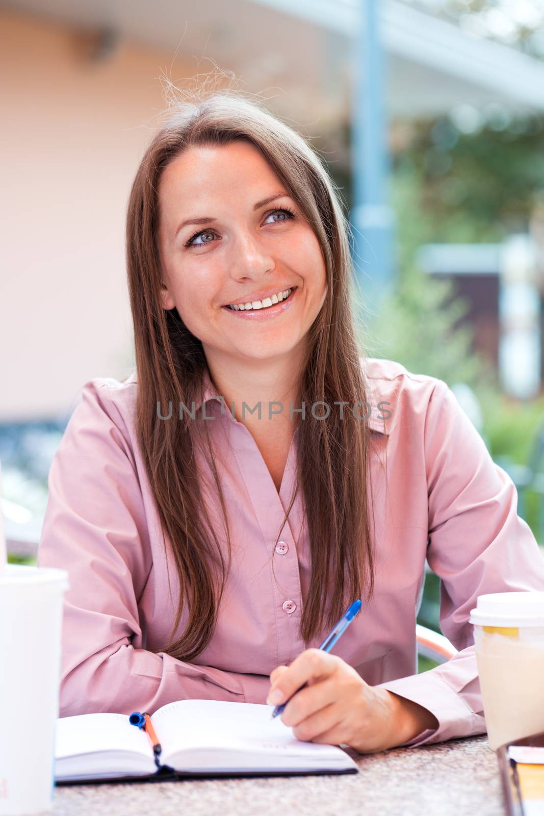 Happy businesswoman sitting in a cafe and writing in organizer