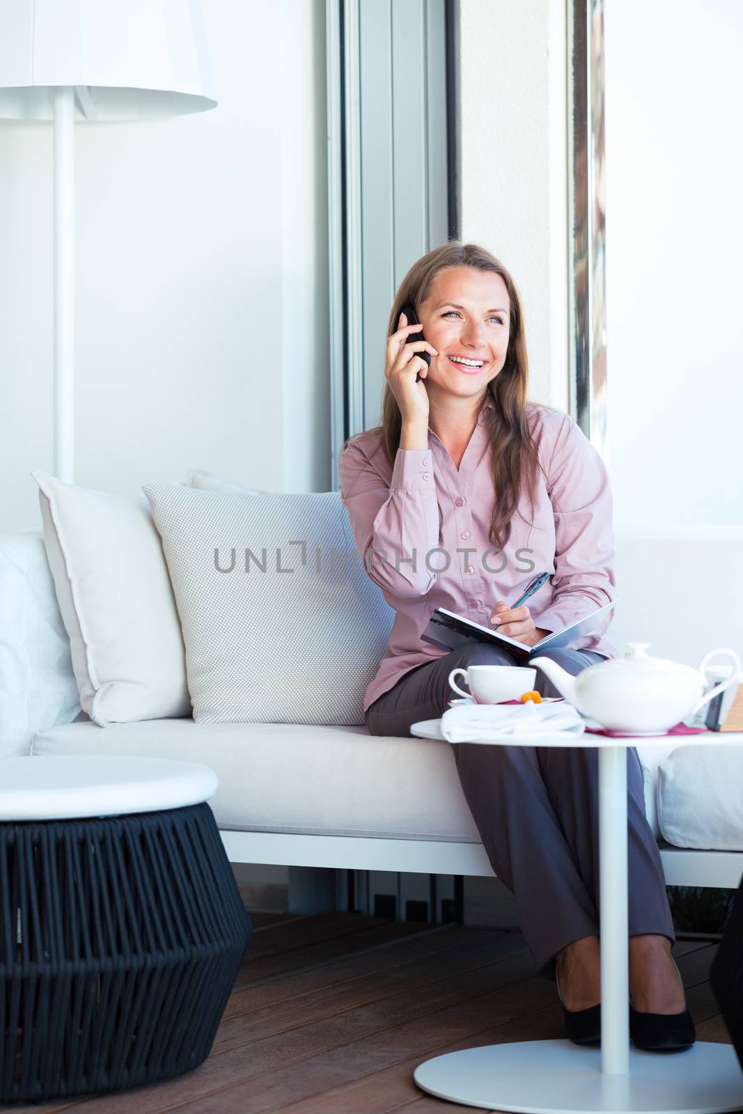 Happy businesswoman talking on the phone and writing in organizer in a coffee shop