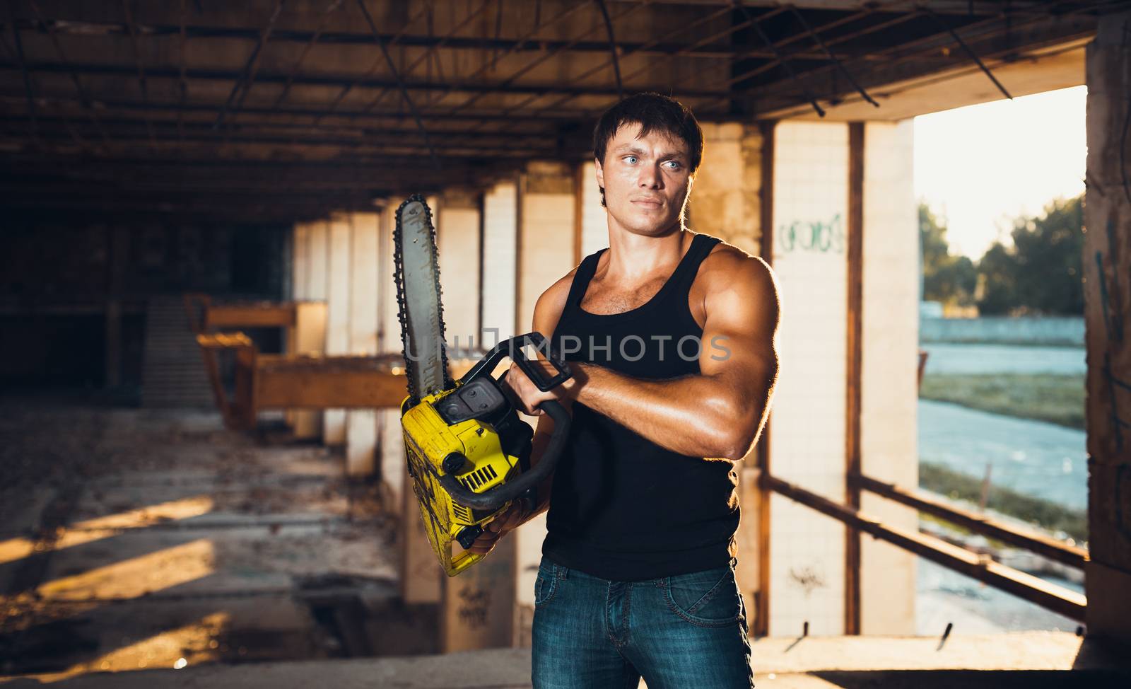 Muscular man with a chainsaw on the ruins