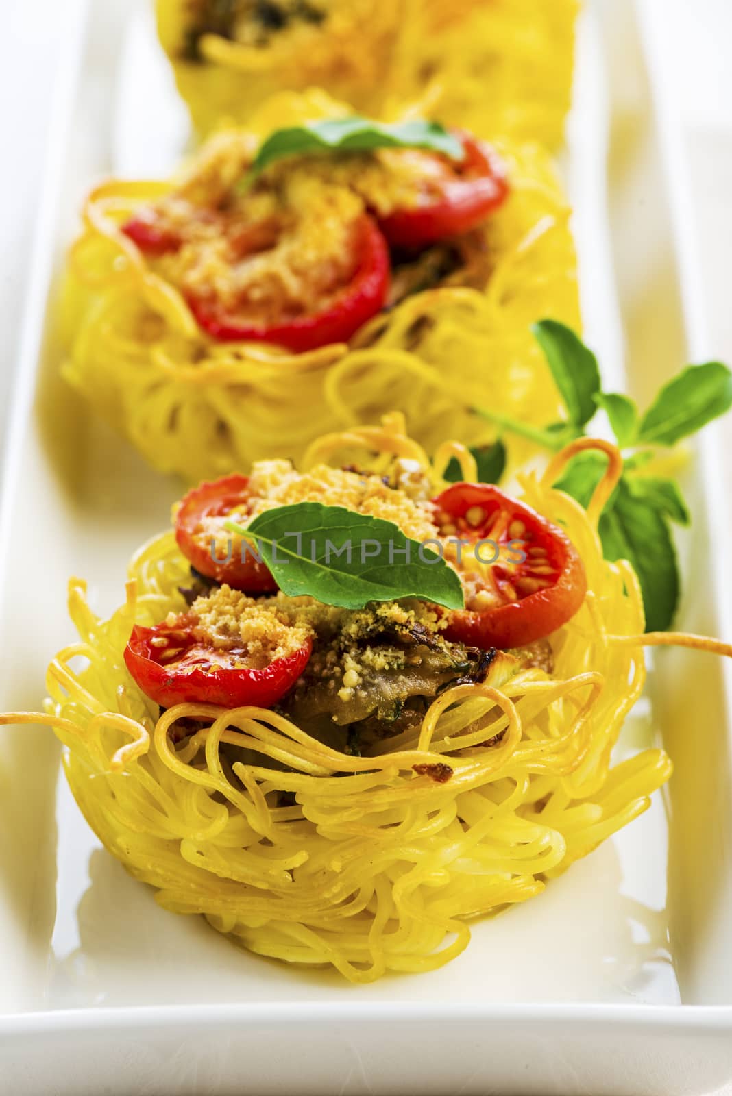 pasta nest arranged on a white porcelain plate with tomatoes parmesan and some leaves of basil