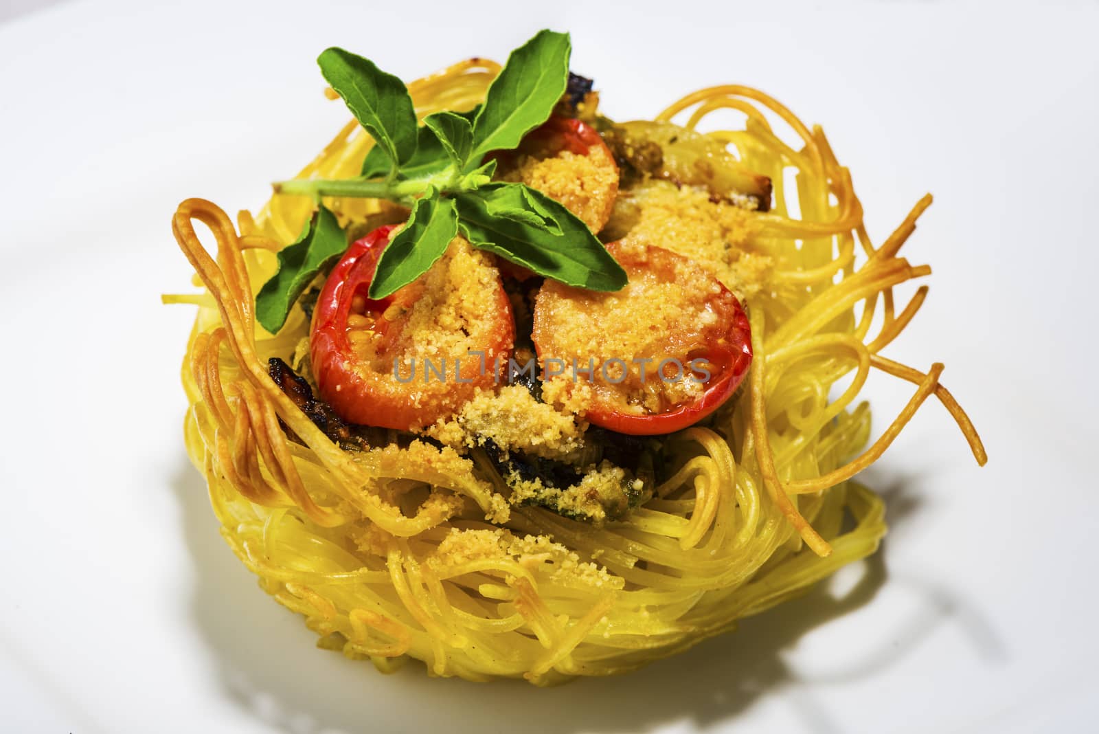 pasta nest arranged on a white porcelain plate with tomatoes parmesan and some leaves of basil