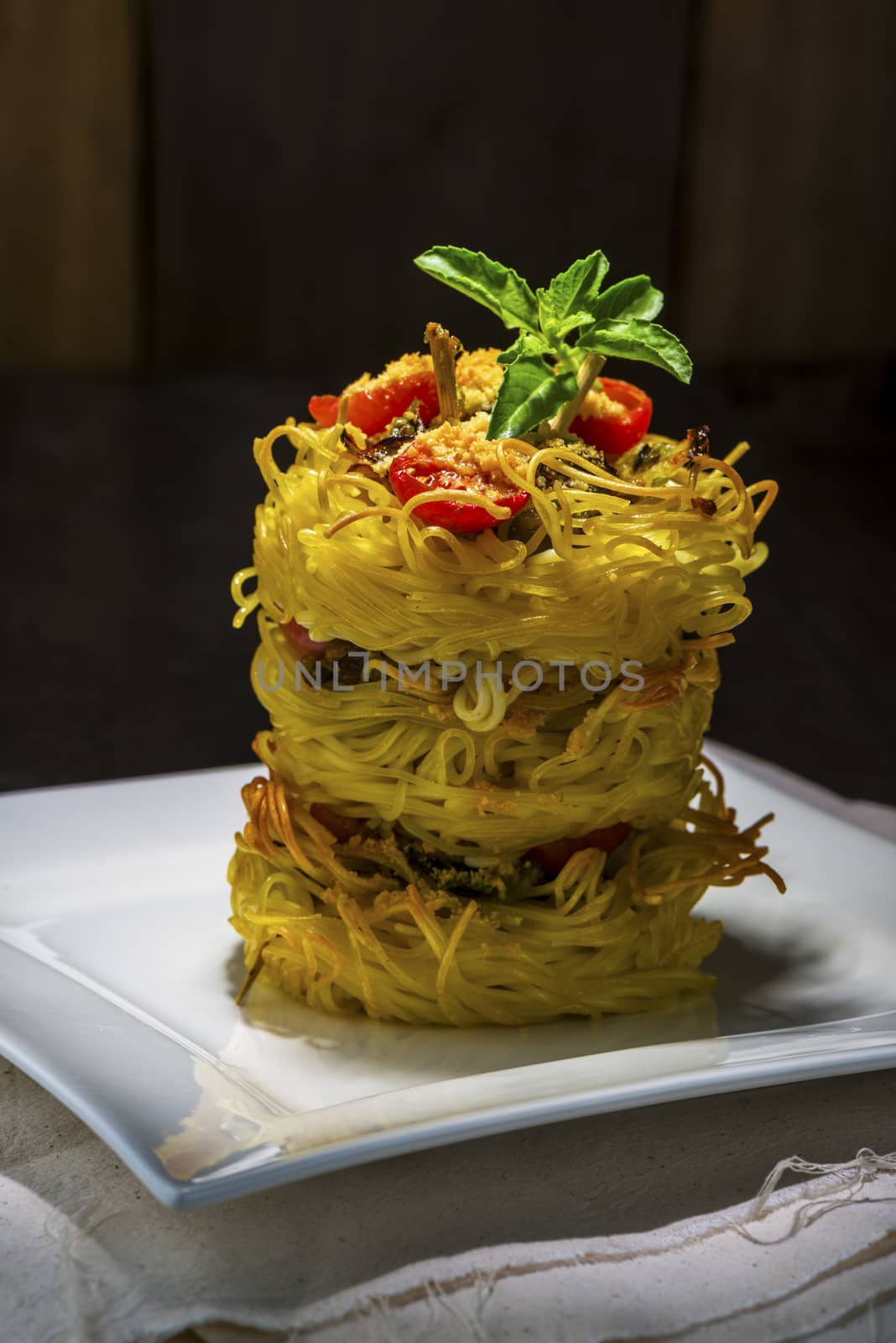 pasta nest arranged on a white porcelain plate with tomatoes parmesan and some leaves of basil