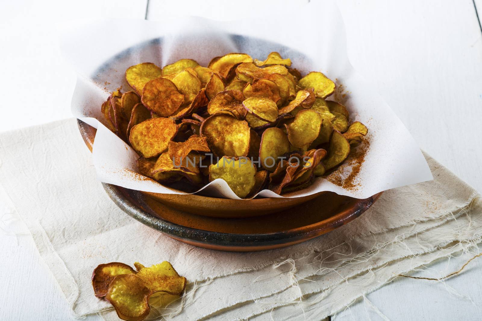 Homemade sweet potatoes chips in a rustic clay plate on white wood table