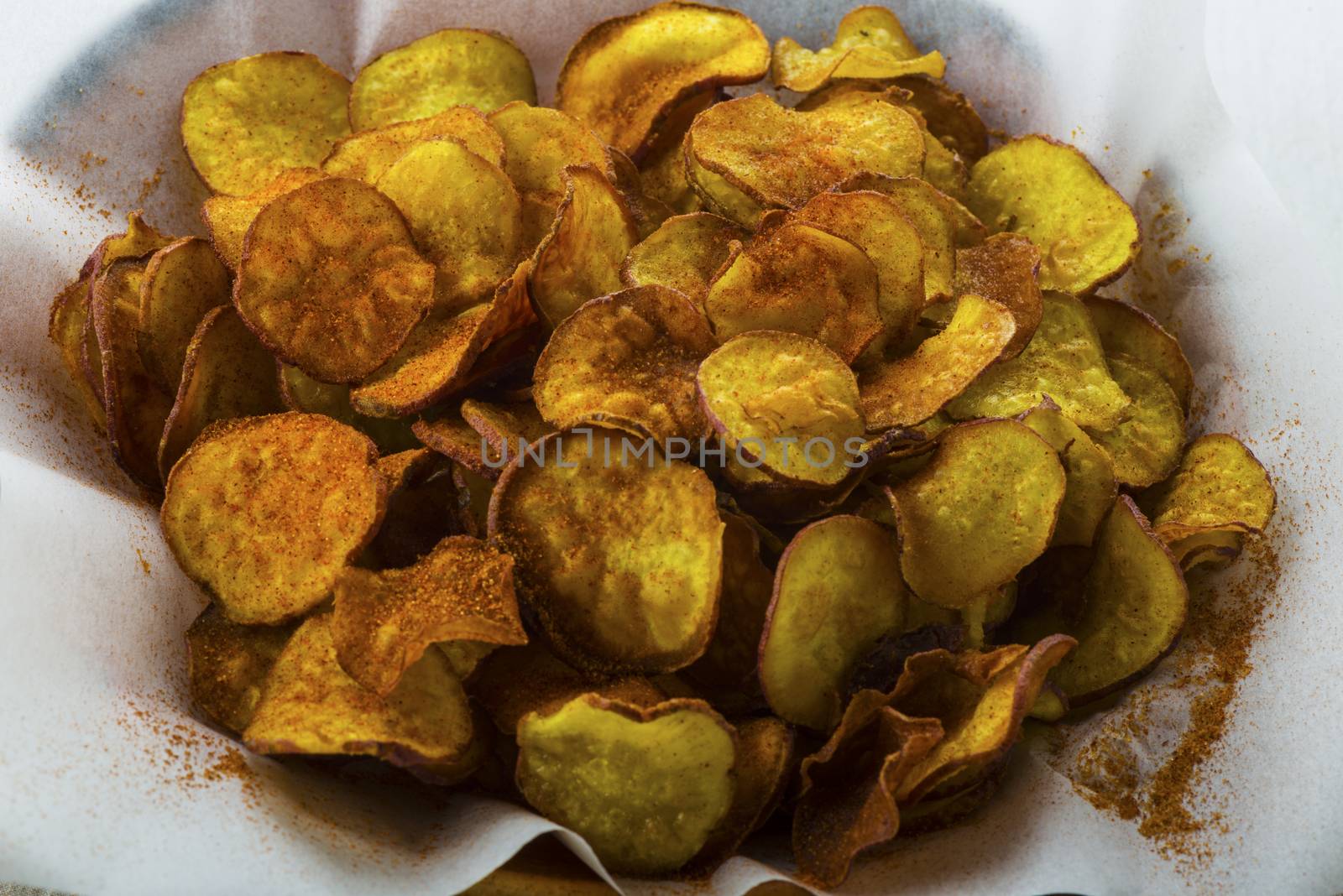 Homemade sweet potatoes chips in a rustic clay plate on white wood table