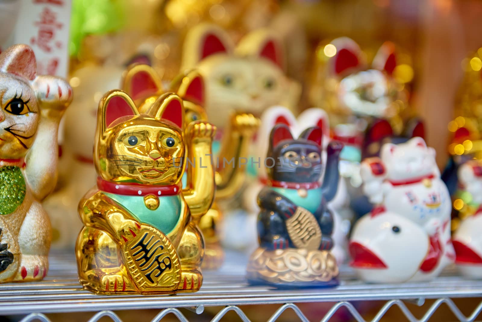 Several traditional Japanese waving cats, with a golden one in focus and the others in the blurred background.