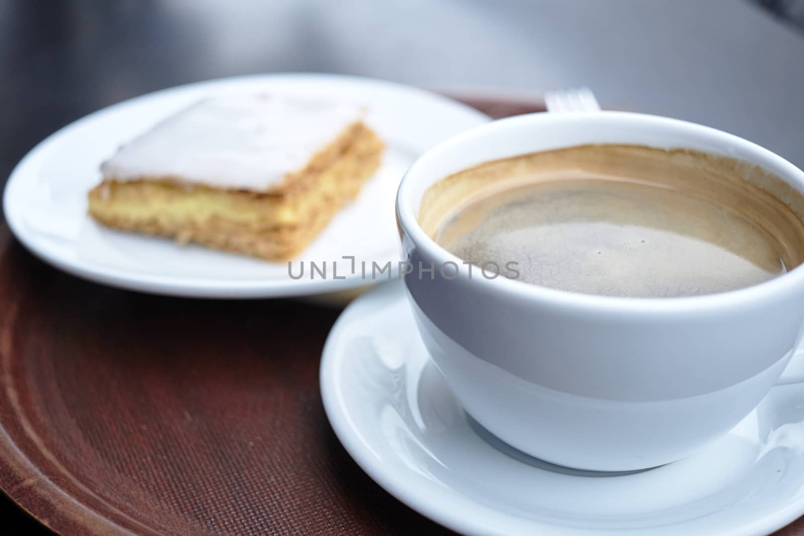 Shallow depth of field shot of coffee cup with mille feuille in the blurred background