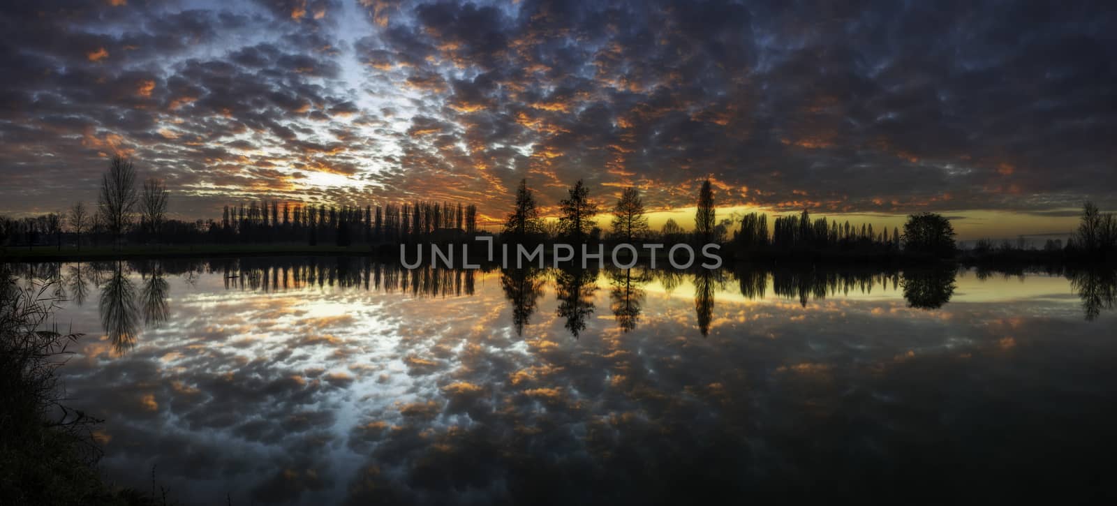 Winter sunset in the shore of a lake with clouds reflected in th by enrico.lapponi