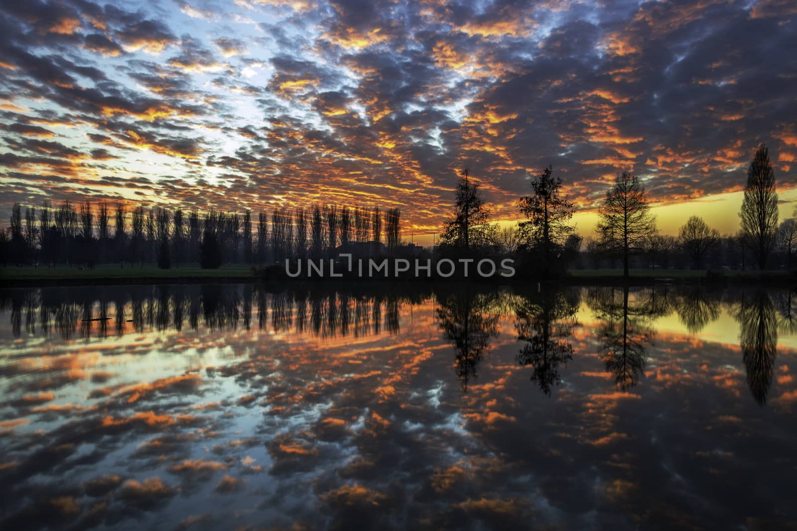 Winter sunset in the shore of a lake with clouds reflected in the water