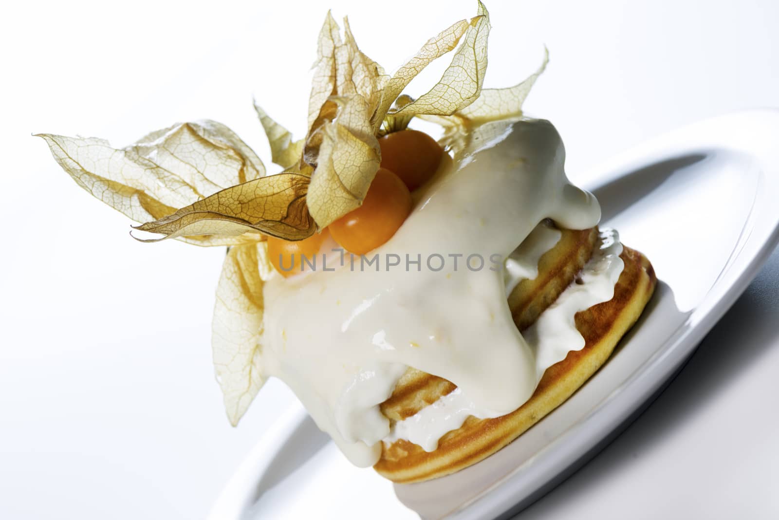 a stack of pancakes with cream and decorated with physalis on white background