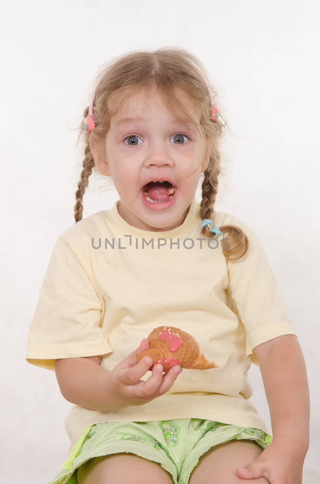 Three year old girl with pigtails and funny enthusiastically eating a bun