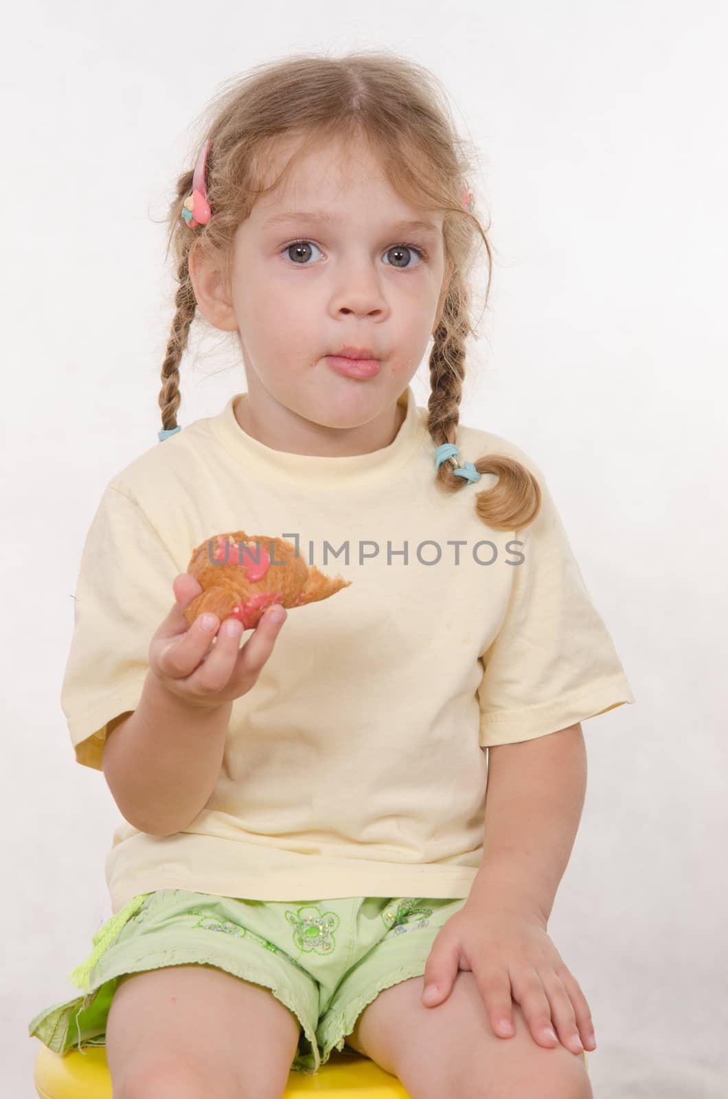 Three year old girl with pigtails and funny enthusiastically eating a bun