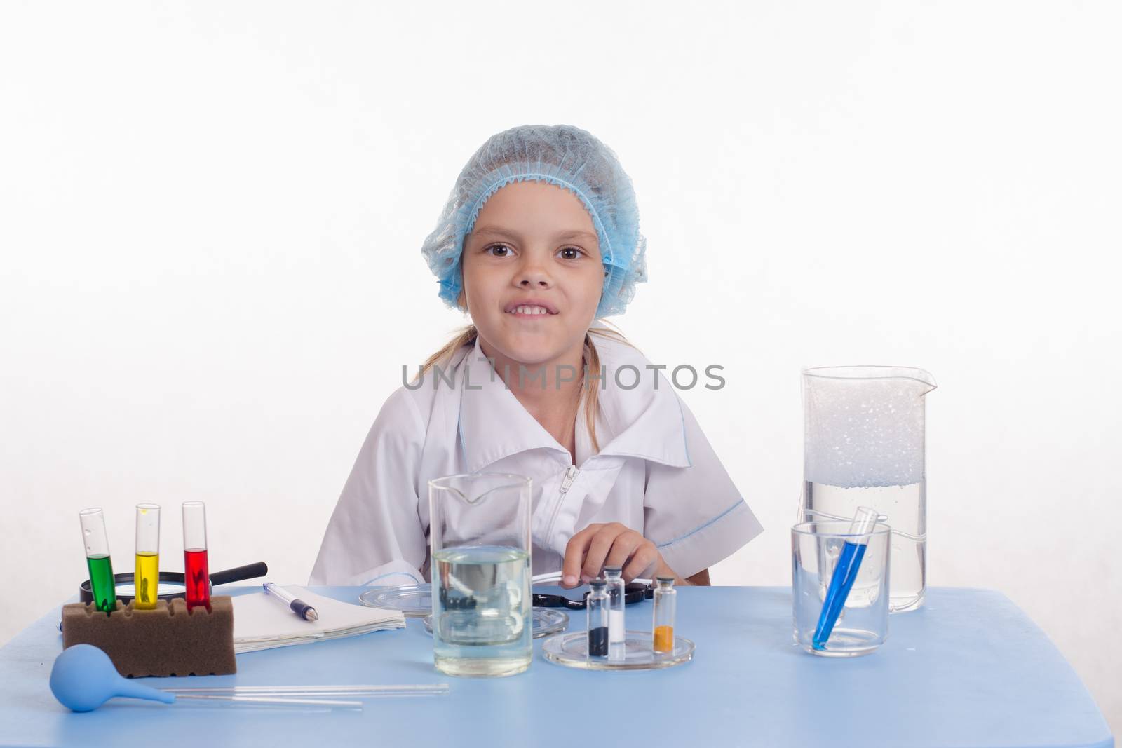 Chemist girl sitting at the table with the reagents in chemistry class and puts experiments