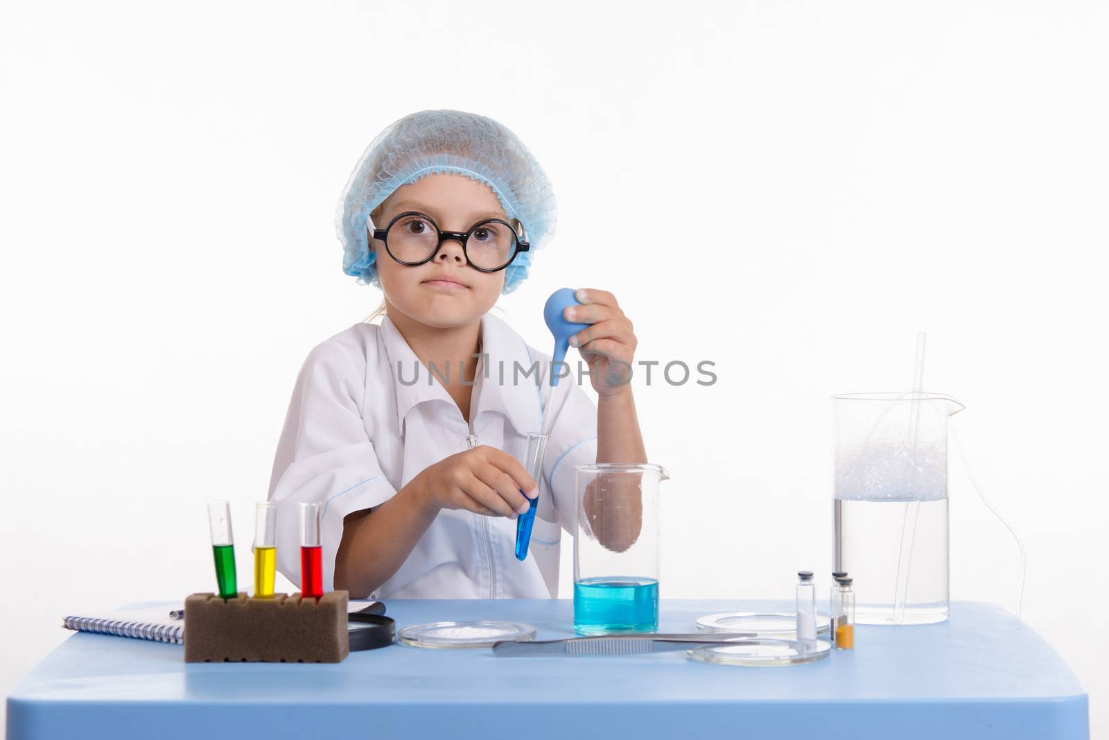 Chemist girl sitting at the table with the reagents in chemistry class and puts experiments