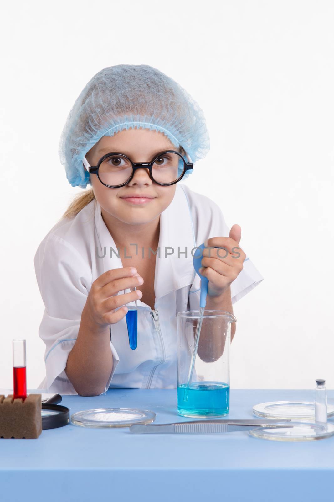 Chemist girl sitting at the table with the reagents in chemistry class and puts experiments