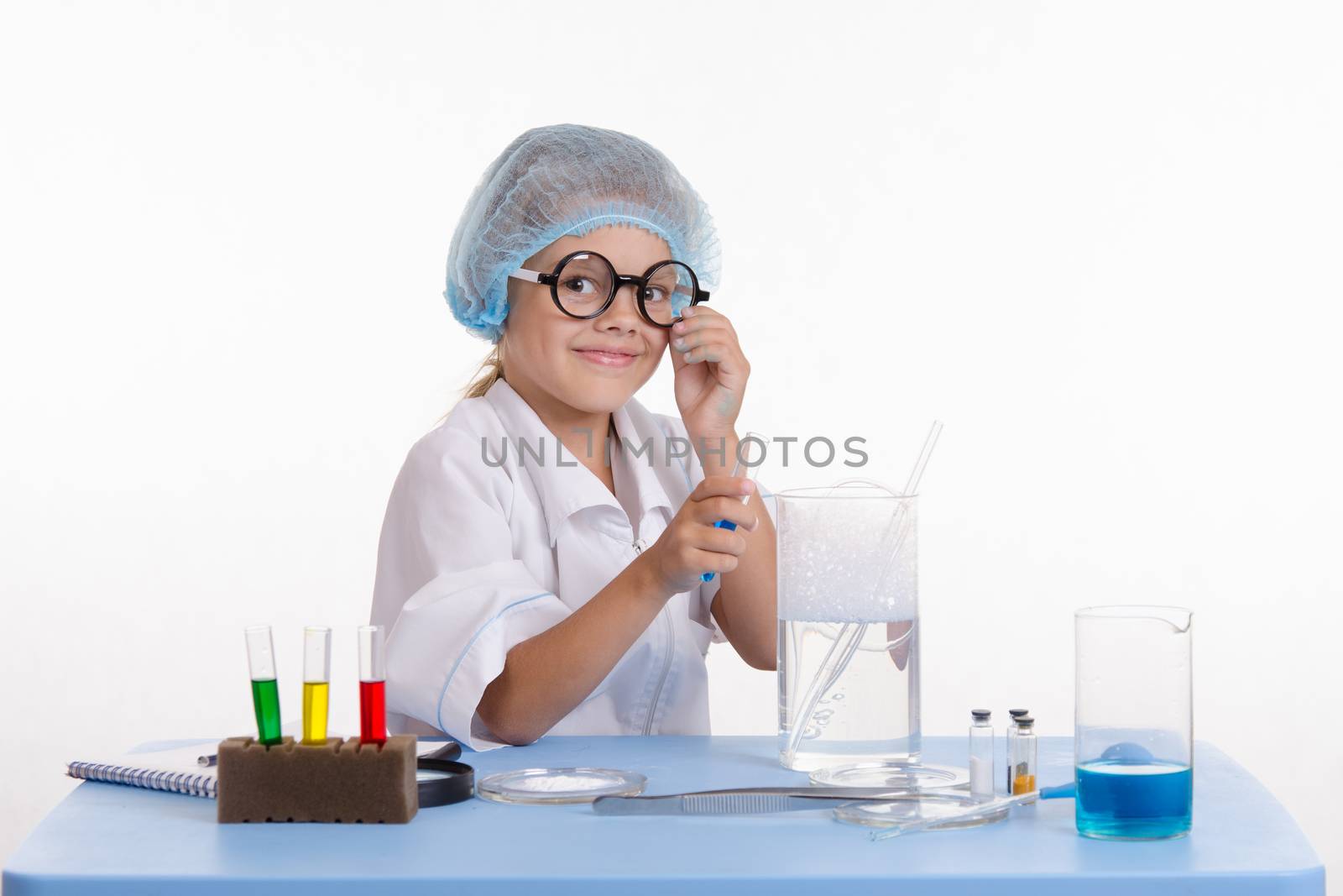Chemist girl sitting at the table with the reagents in chemistry class and puts experiments