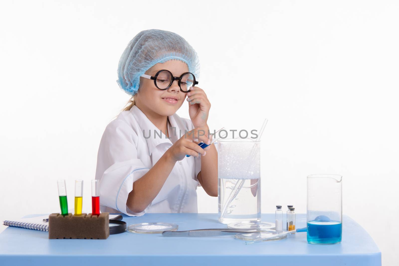 Chemist girl sitting at the table with the reagents in chemistry class and puts experiments