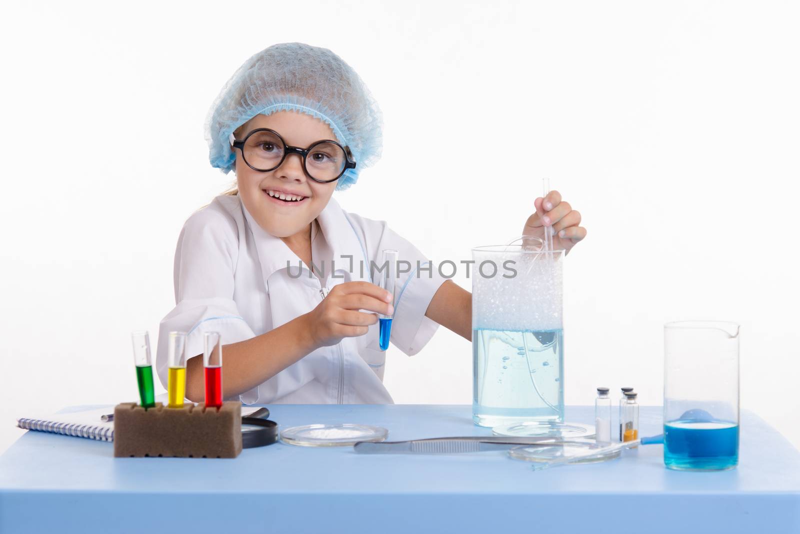 Chemist girl sitting at the table with the reagents in chemistry class and puts experiments