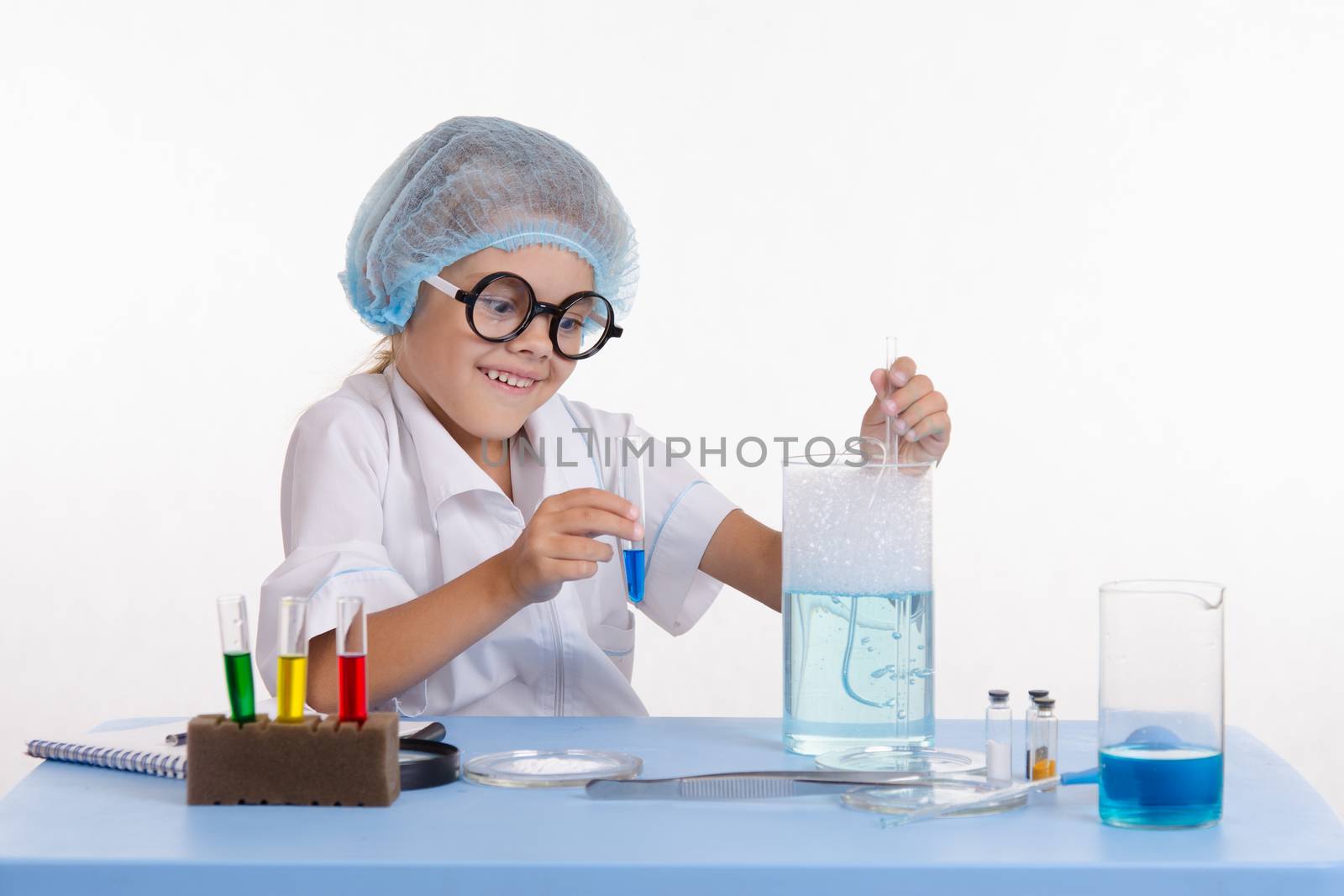 Chemist girl sitting at the table with the reagents in chemistry class and puts experiments