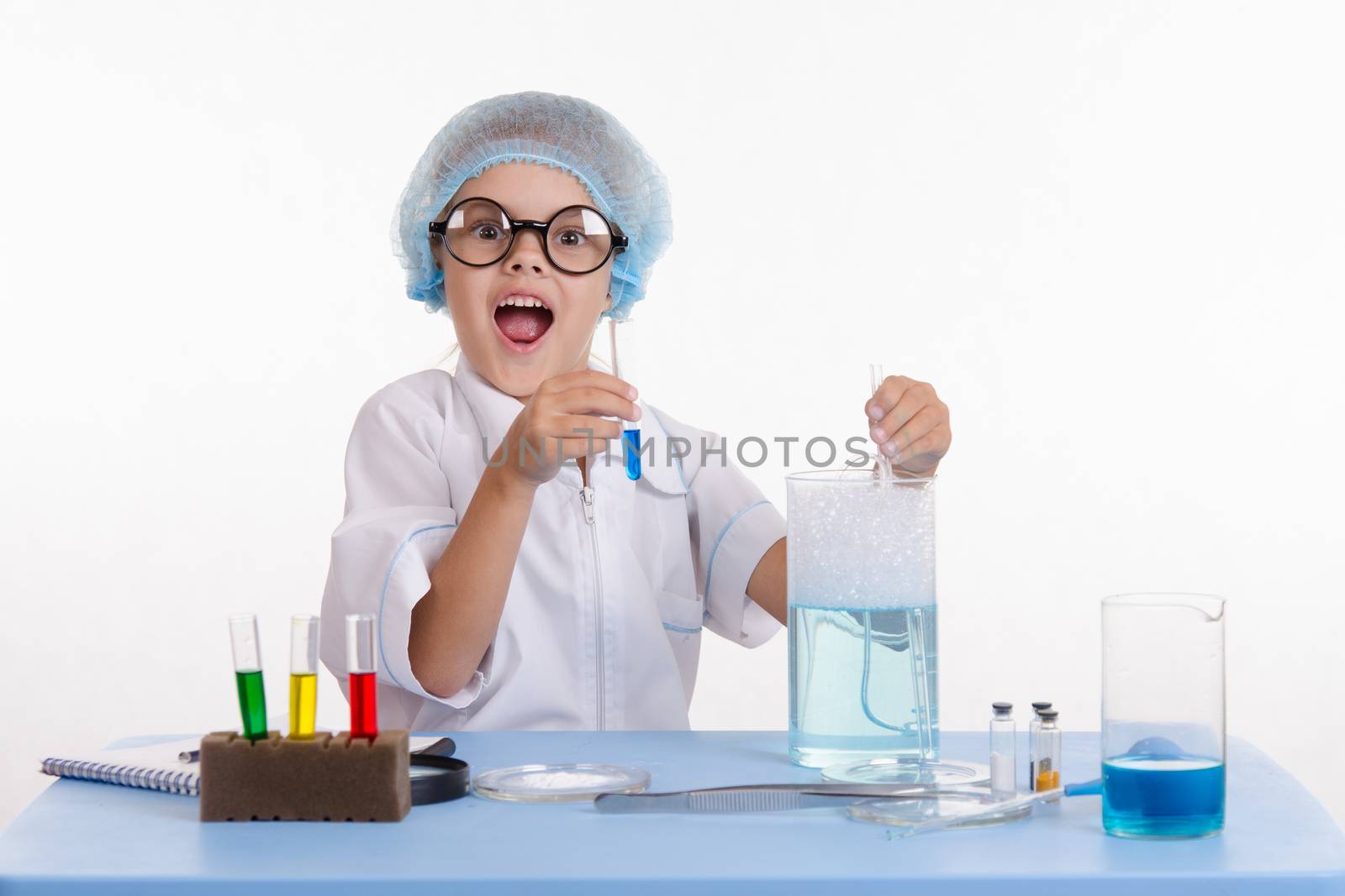 Chemist girl sitting at the table with the reagents in chemistry class and puts experiments