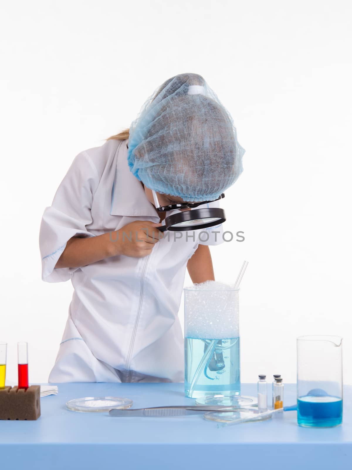 Chemist girl sitting at the table with the reagents in chemistry class and puts experiments