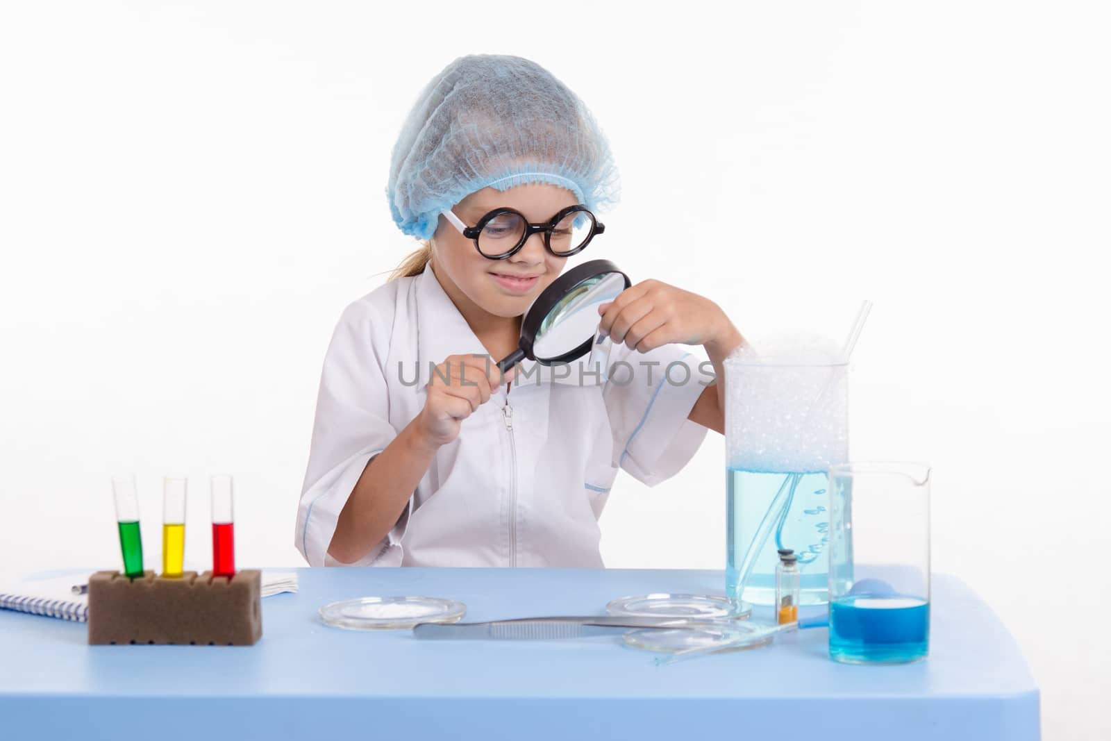 Chemist girl sitting at the table with the reagents in chemistry class and puts experiments